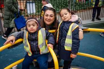 A parent is photographed with two children on a yellow inclusive whirl spinner in the playground. 