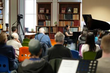 A pianist on a grand piano performing to a crowd in a library