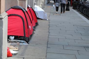 A row of tents to the left of the photo with the back of people walking down the street in the middle 