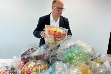 Leader of the Council, Adam Hug, stands in front of lots of bags piled on a table