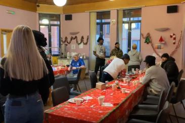 Image shows Look Ahead clients enjoying a Christmas dinner. The table is decorated with a red table cloth, tinsel on the walls and other Christmas decorations including paper Christmas trees and candy canes. 