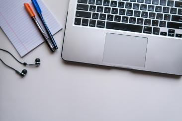 A laptop on a desk, with pens and a notepad