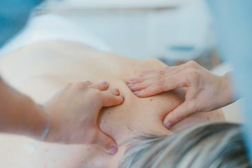 A person is laying down on a massage table and the masseur has both hands on their back