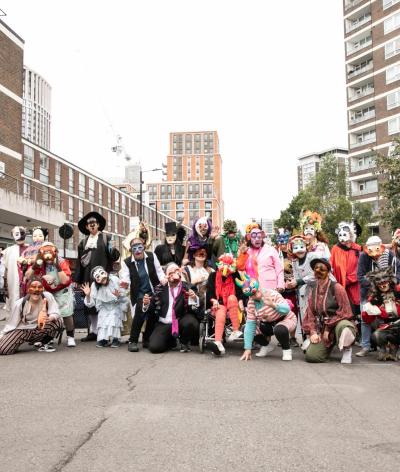 A group of performers in masquerade masks standing in a road on Church Street Market