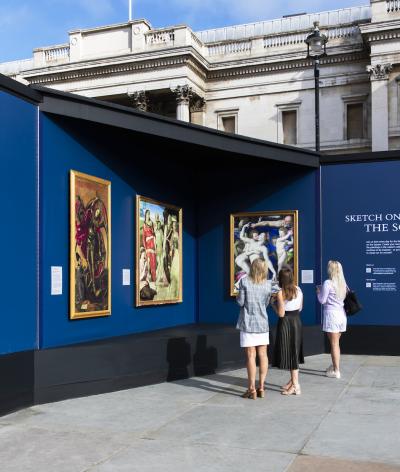  three women looking at a blue signage for the nations favourite images, outside of the National Gallery 