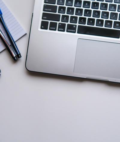 A laptop on a desk, with pens and a notepad