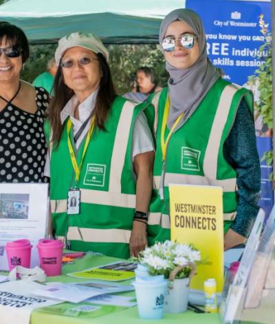 A group of westminster connects volunteers standing behind a branded stall in a park