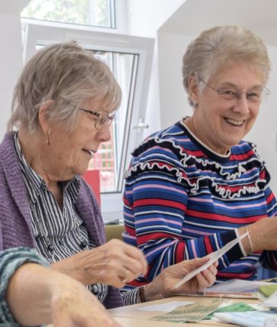 Two women making some cards, sat at a table and surrounded by items to decorate with