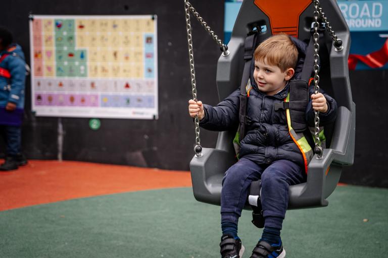 A young person is photographed using an inclusive swing which is designed to provide safety and comfort while swinging. 