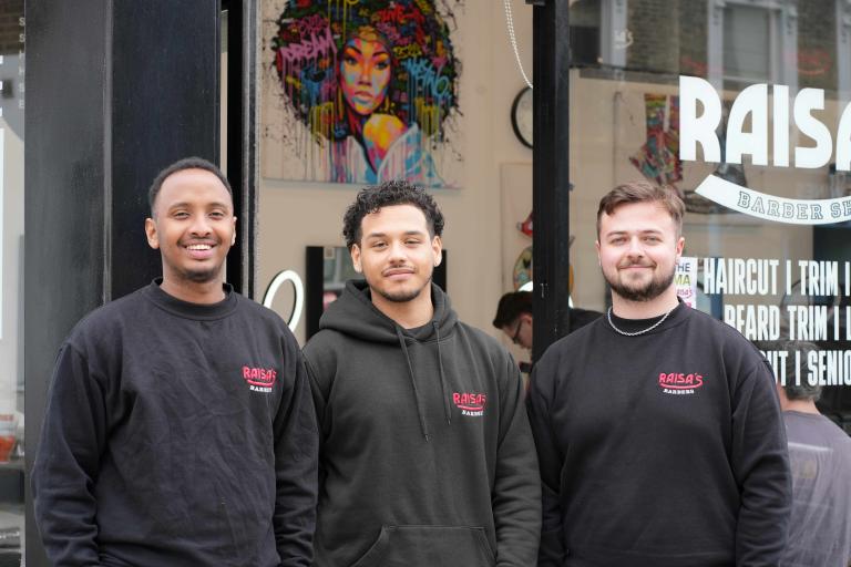 Three barbers standing outside their shop