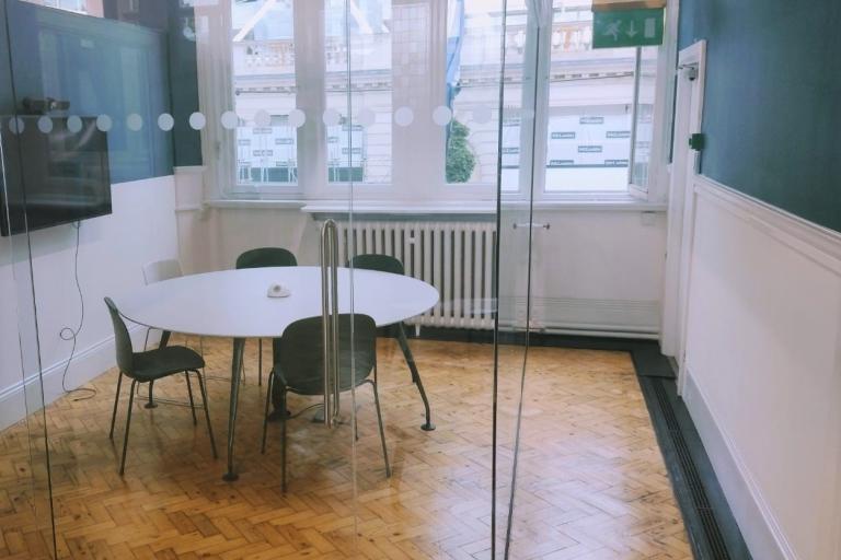 Colour photo of meeting room with 1 round table 4 chairs and 1 screen 