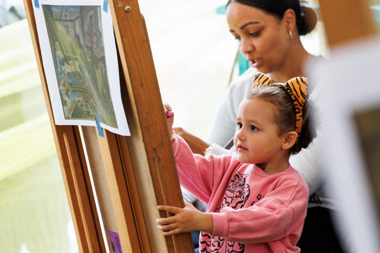 a mother and child painting on an easel 