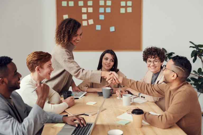 Young people having a meeting with two of them shaking hands across the desk