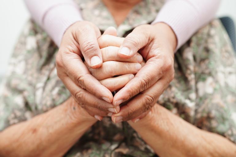 A close-up shot of a carer holding the hands of an elderly person, resembling the shape of a heart.