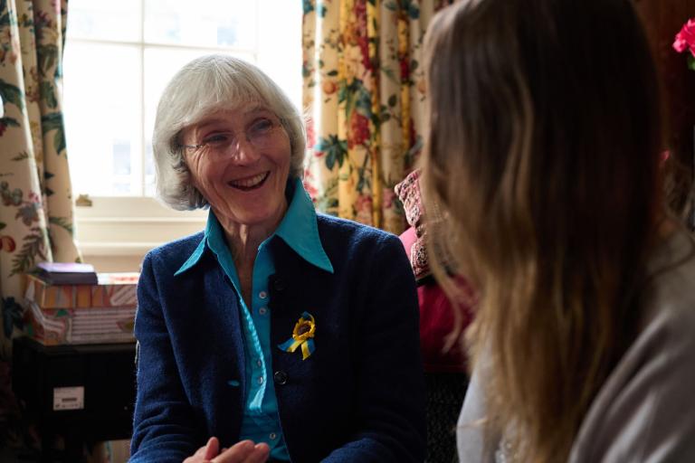 Margaret is sat down on a sofa, looking at someone and smiling