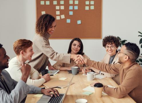 Young people having a meeting with two of them shaking hands across the desk