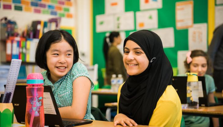 Two children sitting at a desk in a school classroom