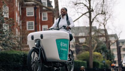 A woman riding a beryl bike on a Westminster street, with flats and trees on the left hand side of the image