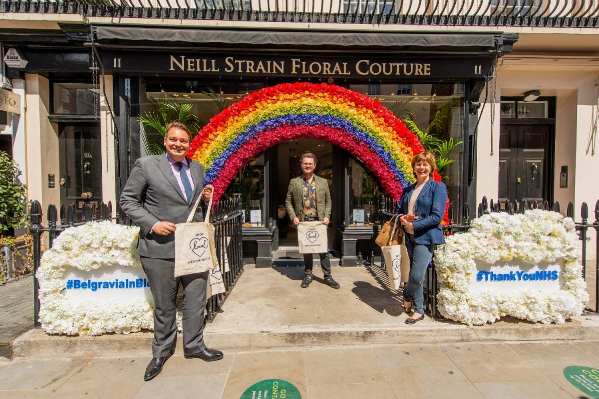 Westminster councillors pose for a photo under a rainbow arch outside a local shop.